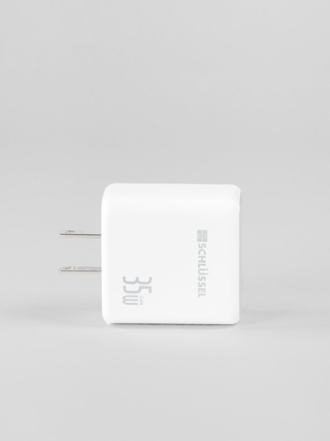 Side profile view of a white Schlüssel 35W GaN wall charger block with two flat metal AC power prongs on the left, shot against a solid light gray background