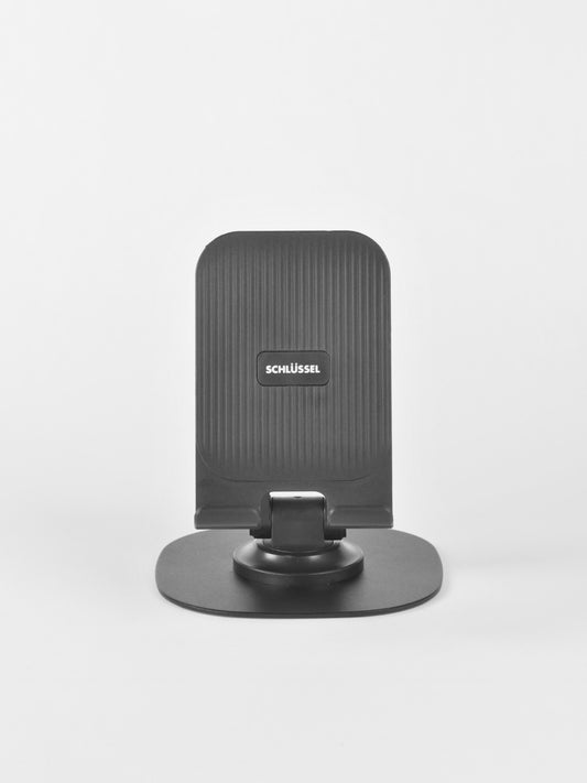 Straight-on front view of the black Schlüssel adjustable desktop phone stand, displaying its vertically ridged backrest, central brand logo, and sturdy base plate against a light gray background